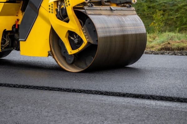 Asphalt road roller with heavy vibration roller compactor press new hot asphalt on the roadway on a road construction site. Heavy Vibration roller at asphalt pavement working.