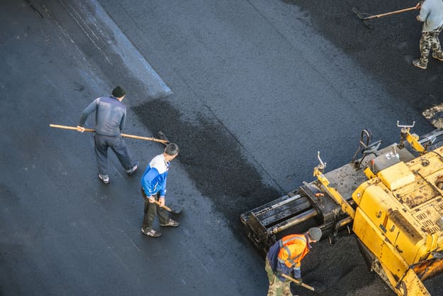 Asphalt workers lay a new asphalt coating using hot bitumen and paver.