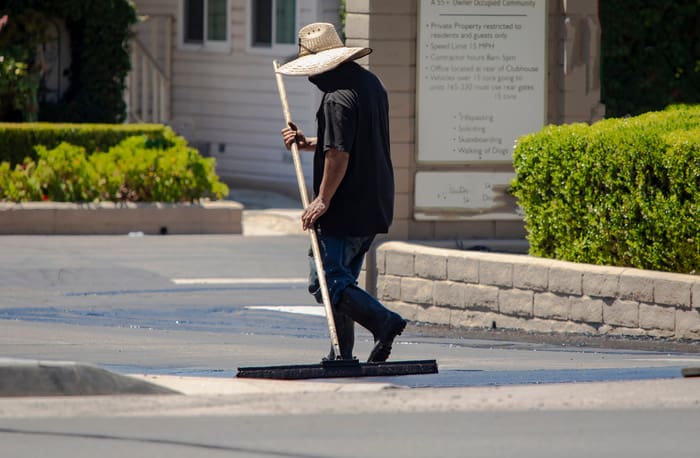 A man in a straw hat spreading new asphalt slurry for sealcoating