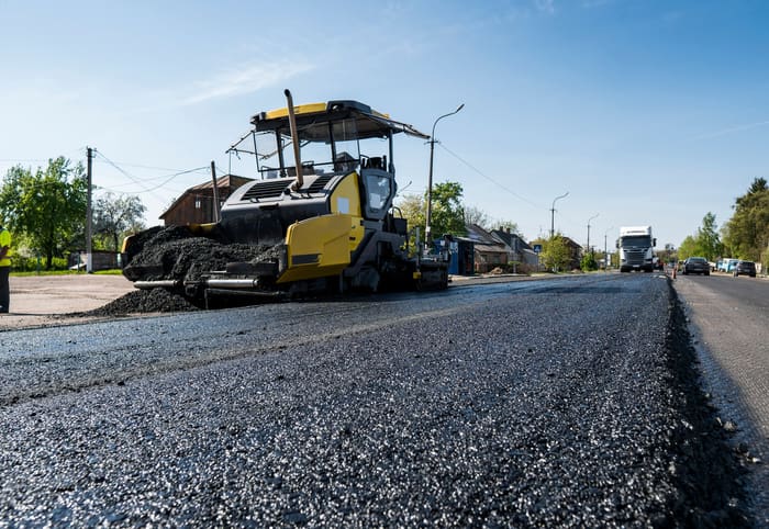 Worker operating asphalt paver machine during road construction and repairing works. A paver finisher, asphalt finisher or paving machine placing a layer of asphalt